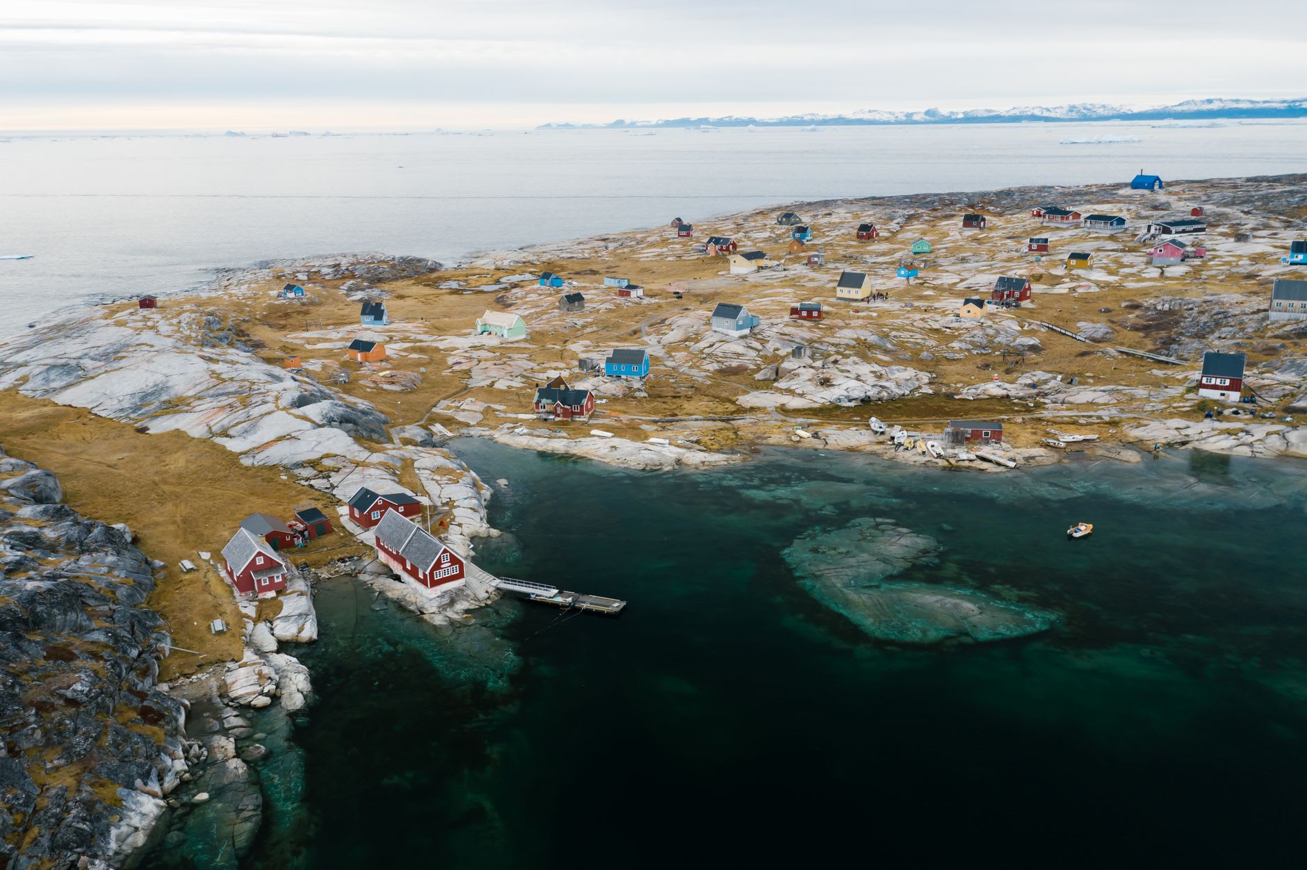 Un cazador inuit comprobando el grosor del hielo en el congelado Fiordo de Ammassalik con luz rosada de la mañana en los picos