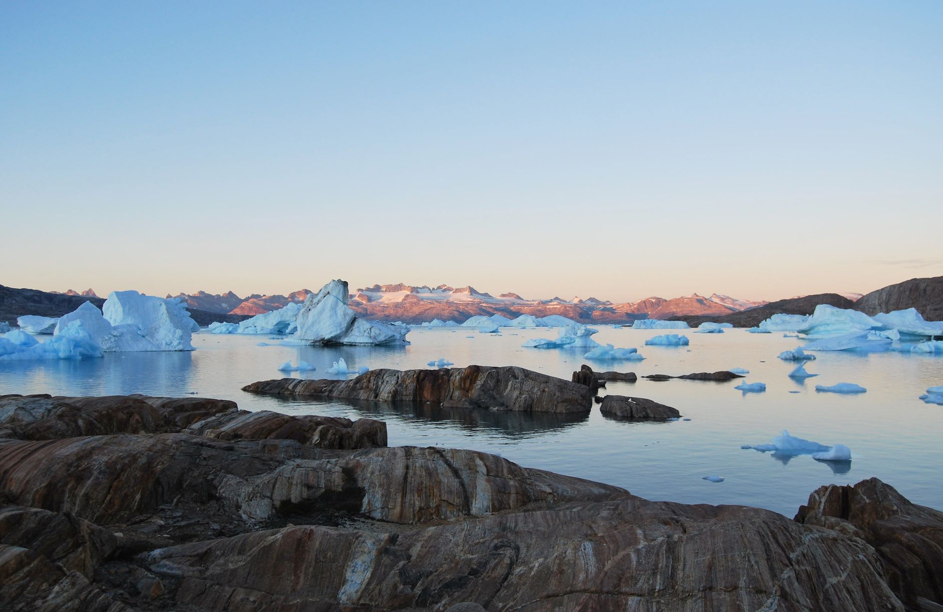 A traditional Greenlandic qajaq pulled up on shore at Tiniteqilaaq with the frozen Sermilik Fjord and towering icebergs behind