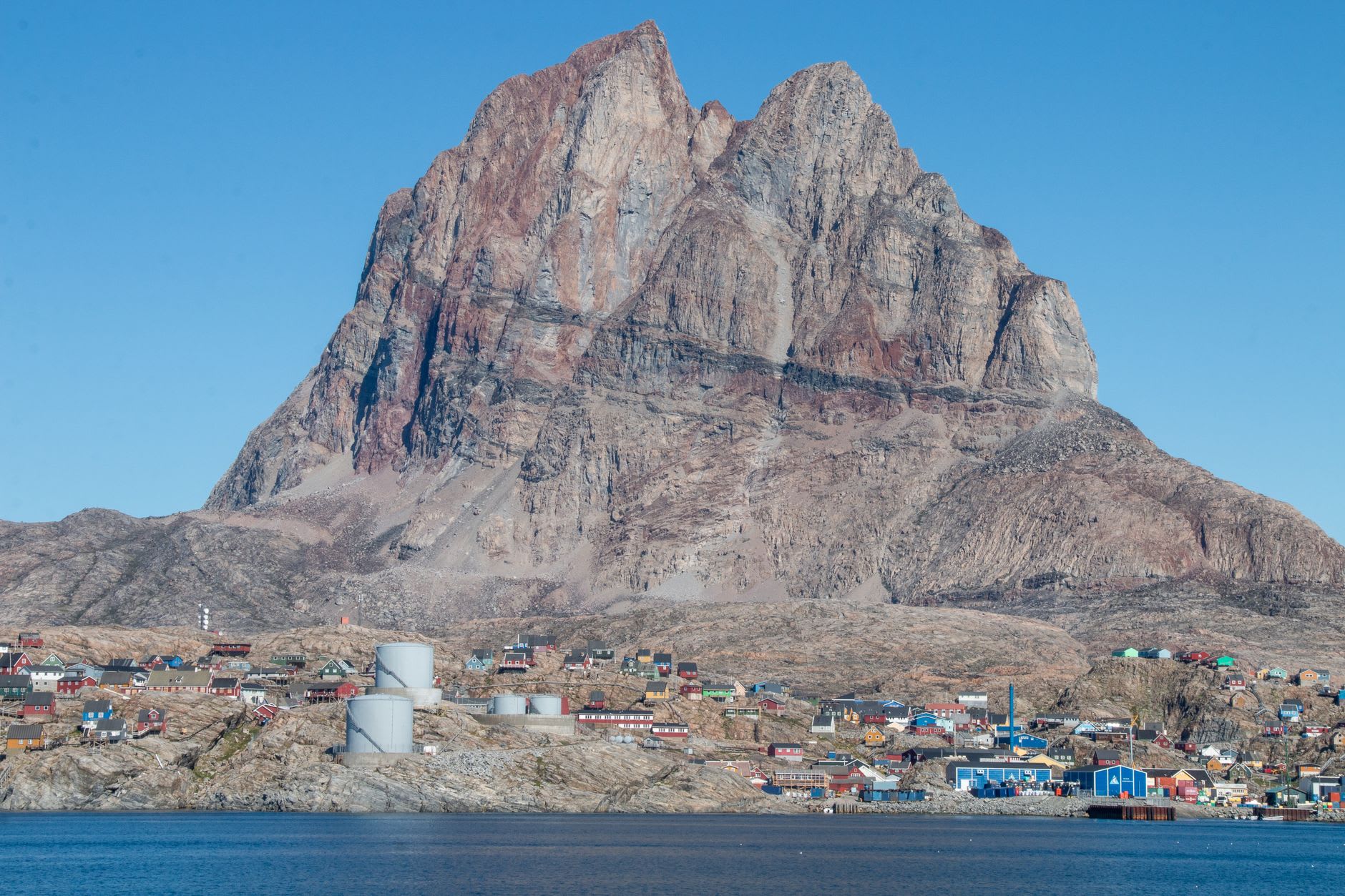 Dog sled team resting on the sea ice of Uummannaq Fjord with the town and its distinctive peak glowing red in the low winter sun