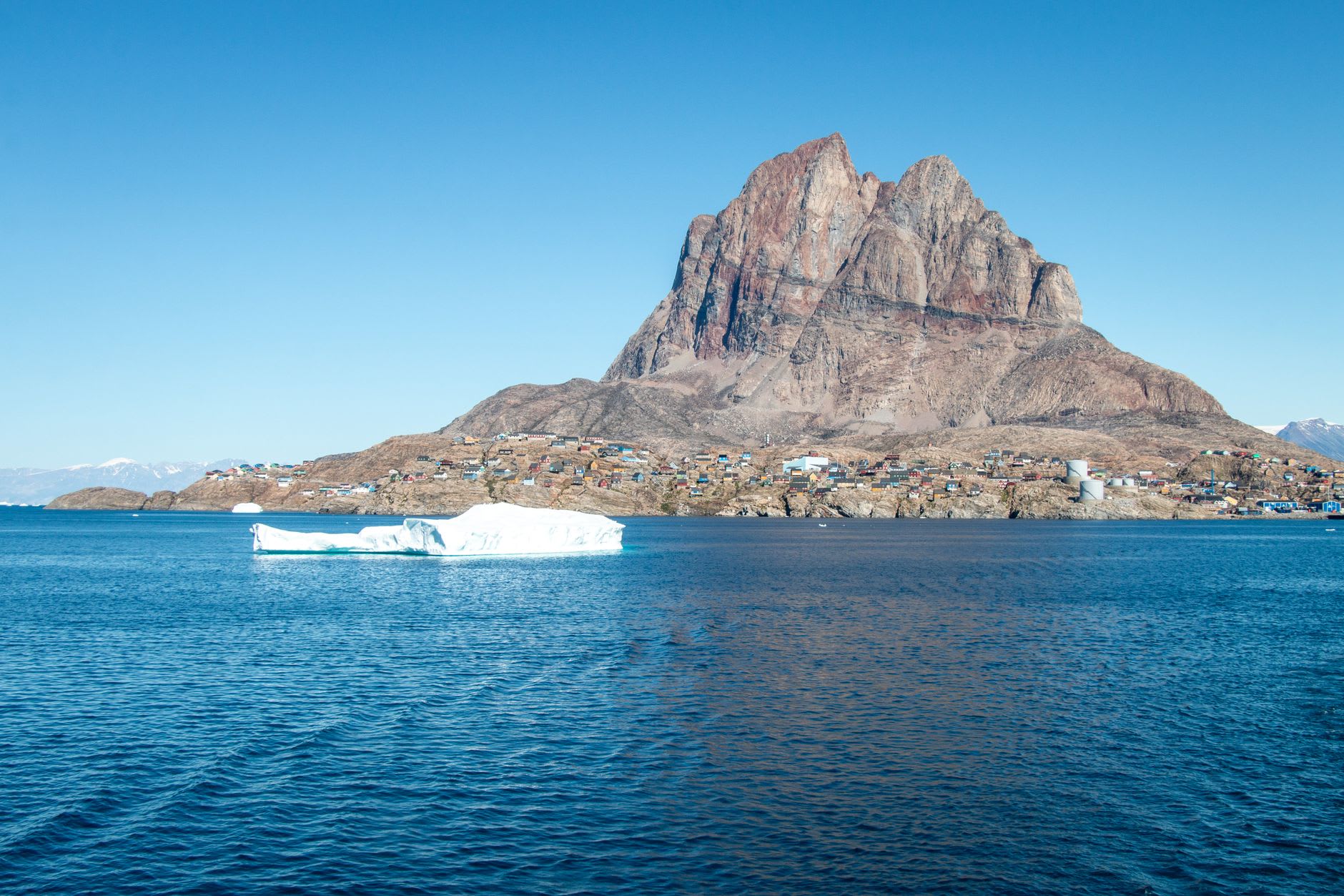 The red gneiss walls of the Uummannaq mountain peak glowing in the low Arctic sun above the frozen fjord