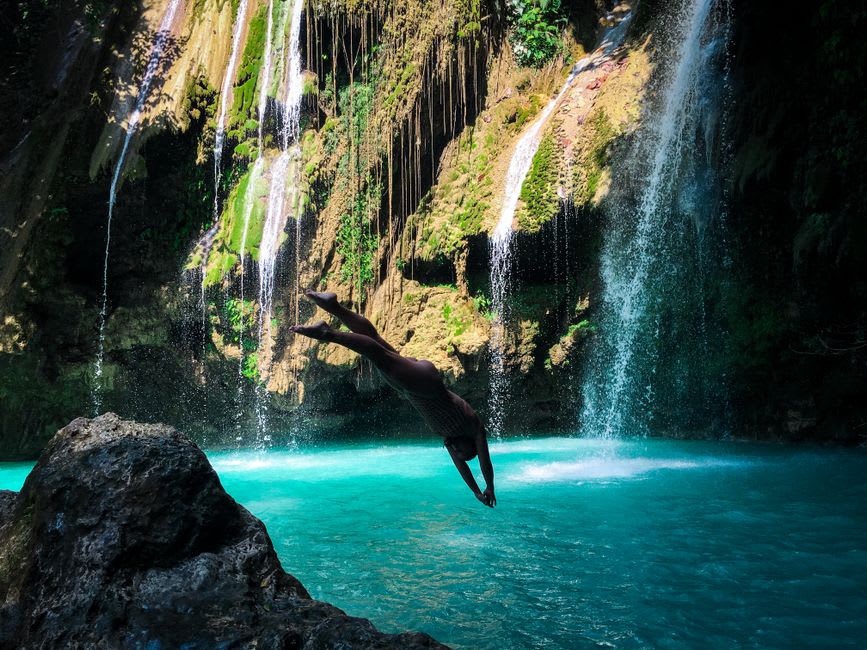 A local guide mid-air cliff diving into the rock pool below Mount Carmel Falls
