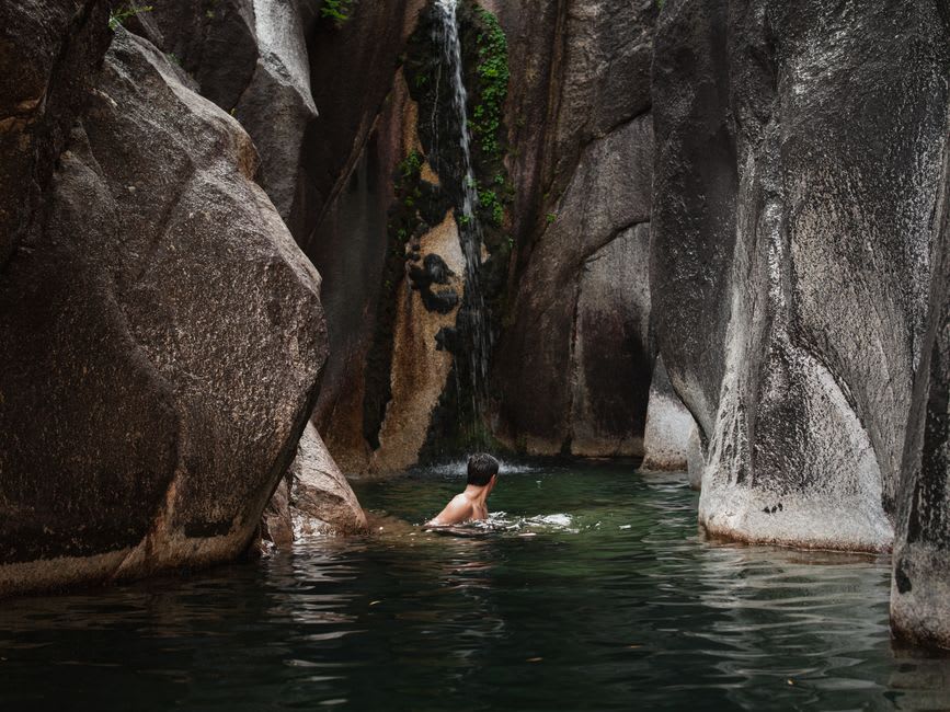 Travelers swimming in a still pool beneath the canyon's shaded cliff walls