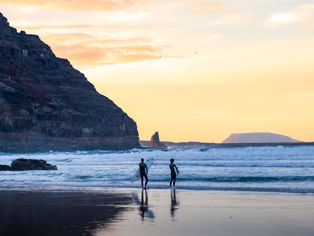 Surfers walking along the black volcanic sand beach at El Paredón, Guatemala, with waves breaking behind them