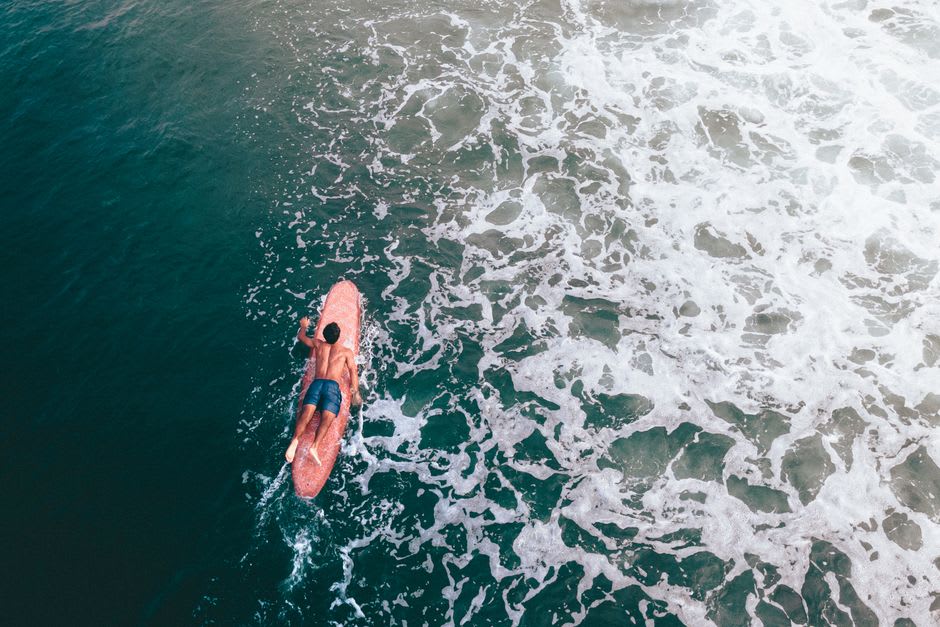 A surf instructor and student paddling out through small waves at El Paredón beach at golden hour