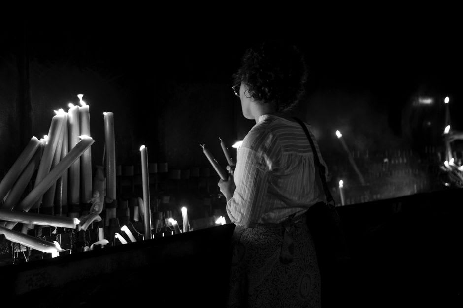 Pilgrims lighting candles and kneeling in prayer before the Black Christ inside the basilica