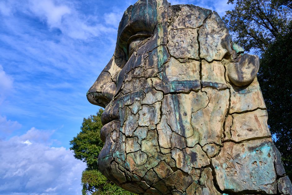 A massive Olmec-influenced stone head carving standing among palm trees in the town plaza