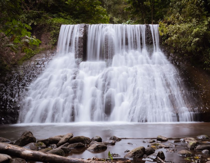 A waterfall of hot spring water pouring over jungle rocks into a cool pool at Finca El Paraíso near Lago de Izabal
