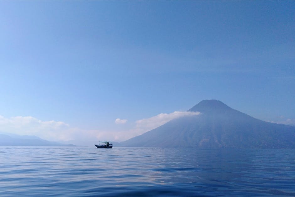 Lake Atitlán at sunrise with three volcanic peaks and mist hovering over the calm water