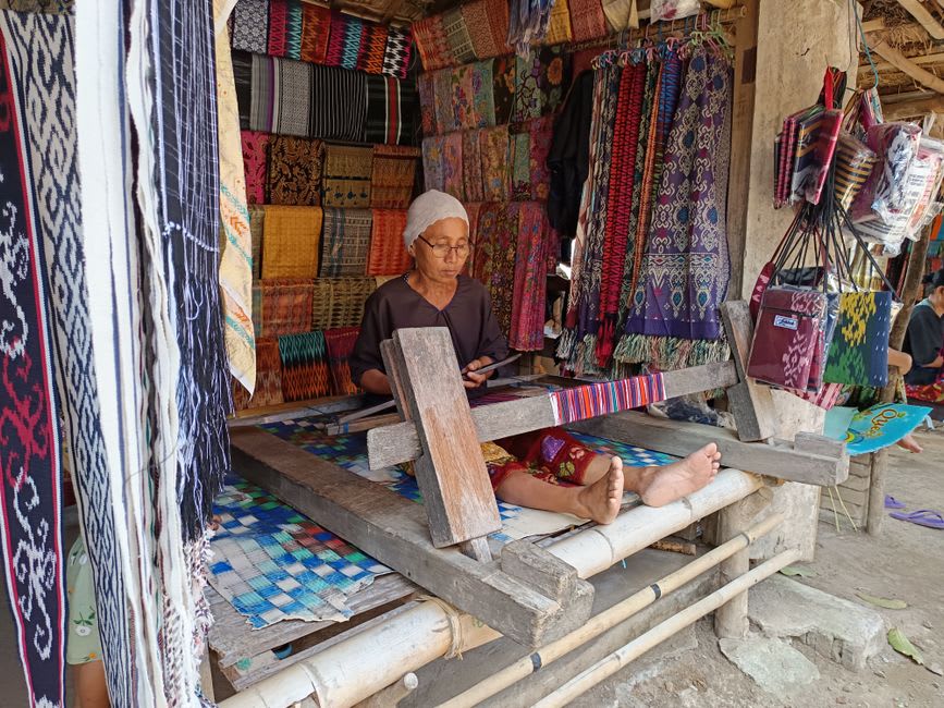 Weaver arranging stacks of grey and cream wool ponchos at the Momostenango market