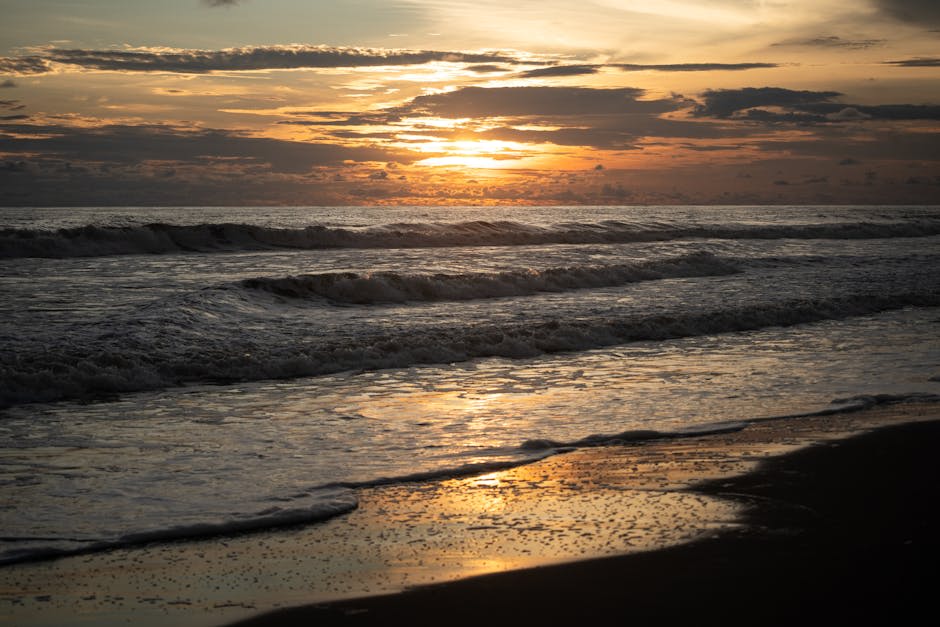 Dramatic Pacific sunset over dark volcanic sand beach with ocean waves