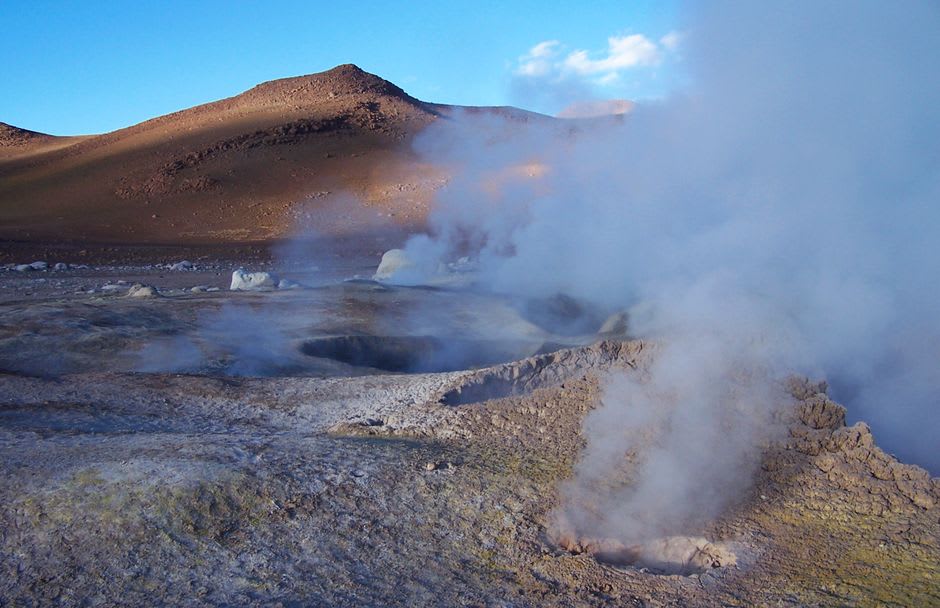 Steam vents rising from the black lava field with volcanoes visible in the distance