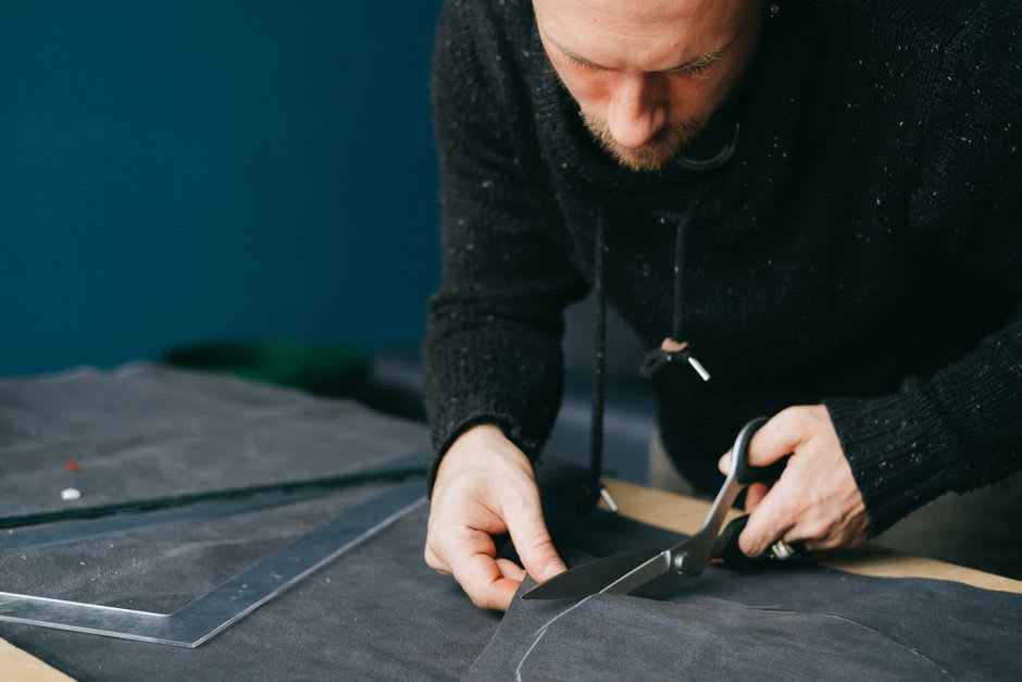 Un artisan du cuir à Pastores découpant un patron de botte dans une peau, avec des outils disposés sur son établi