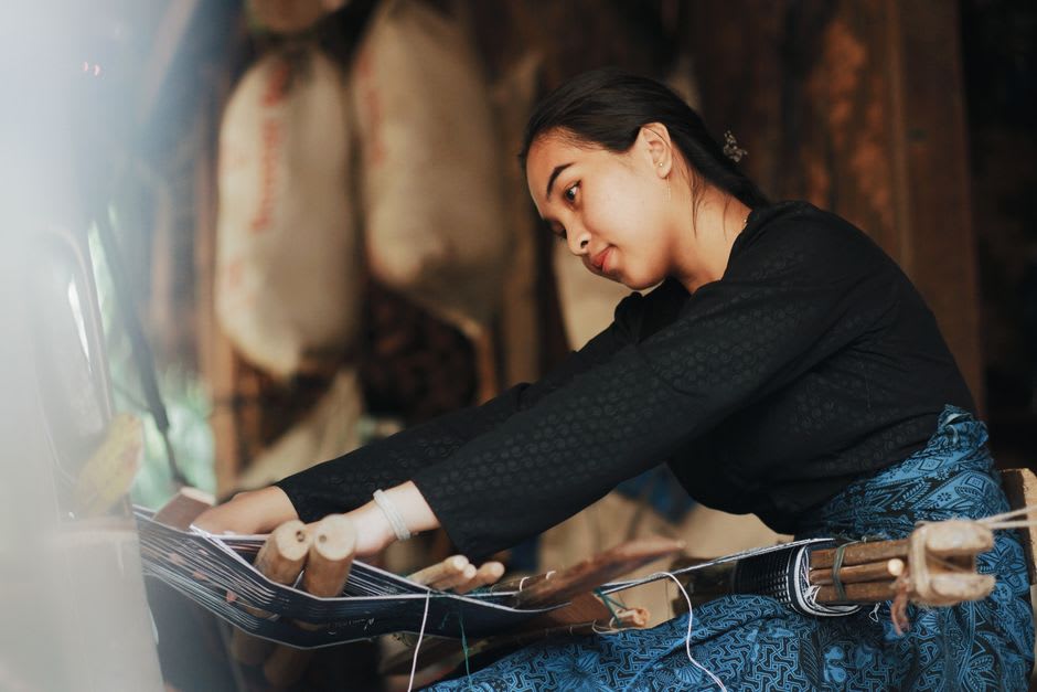 A Kaqchikel woman weaving on a backstrap loom in a courtyard in Santa María de Jesús, with textiles hanging behind her