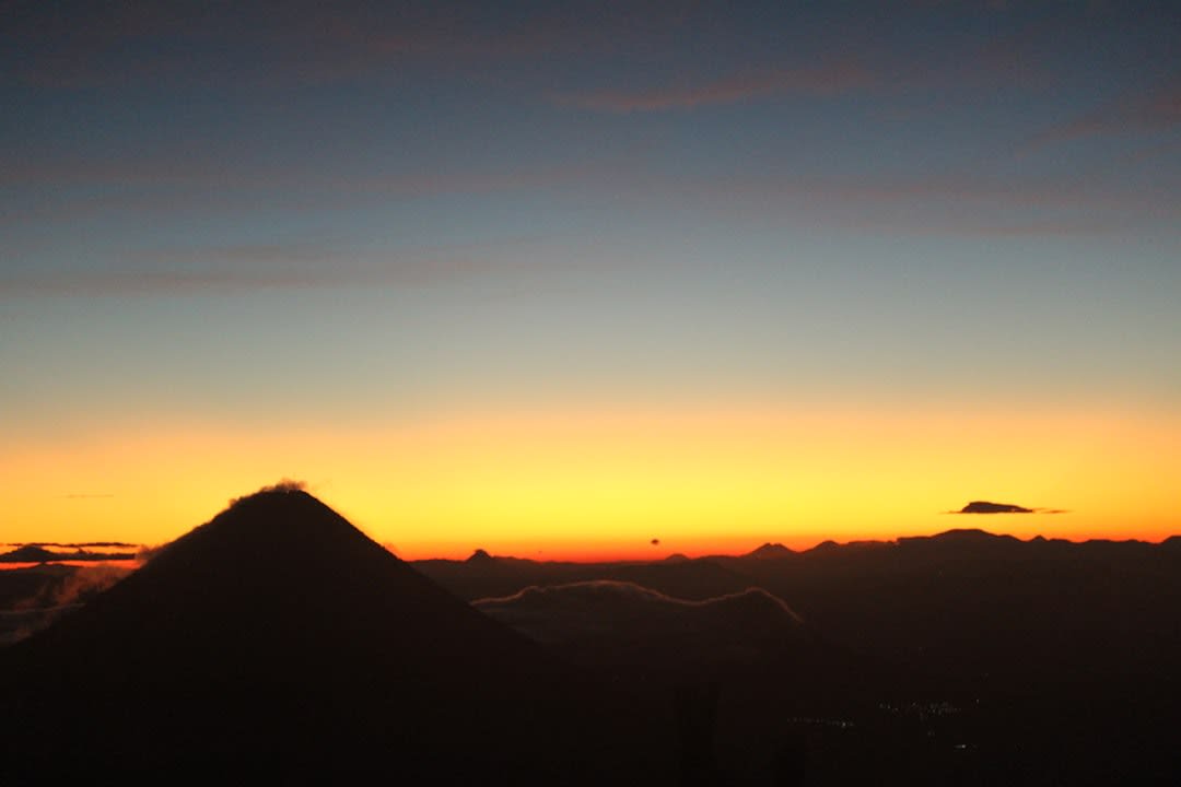 Le rebord du cratère du Volcán de Agua au lever du soleil, avec une mer de nuages en contrebas et d'autres pics volcaniques visibles au loin