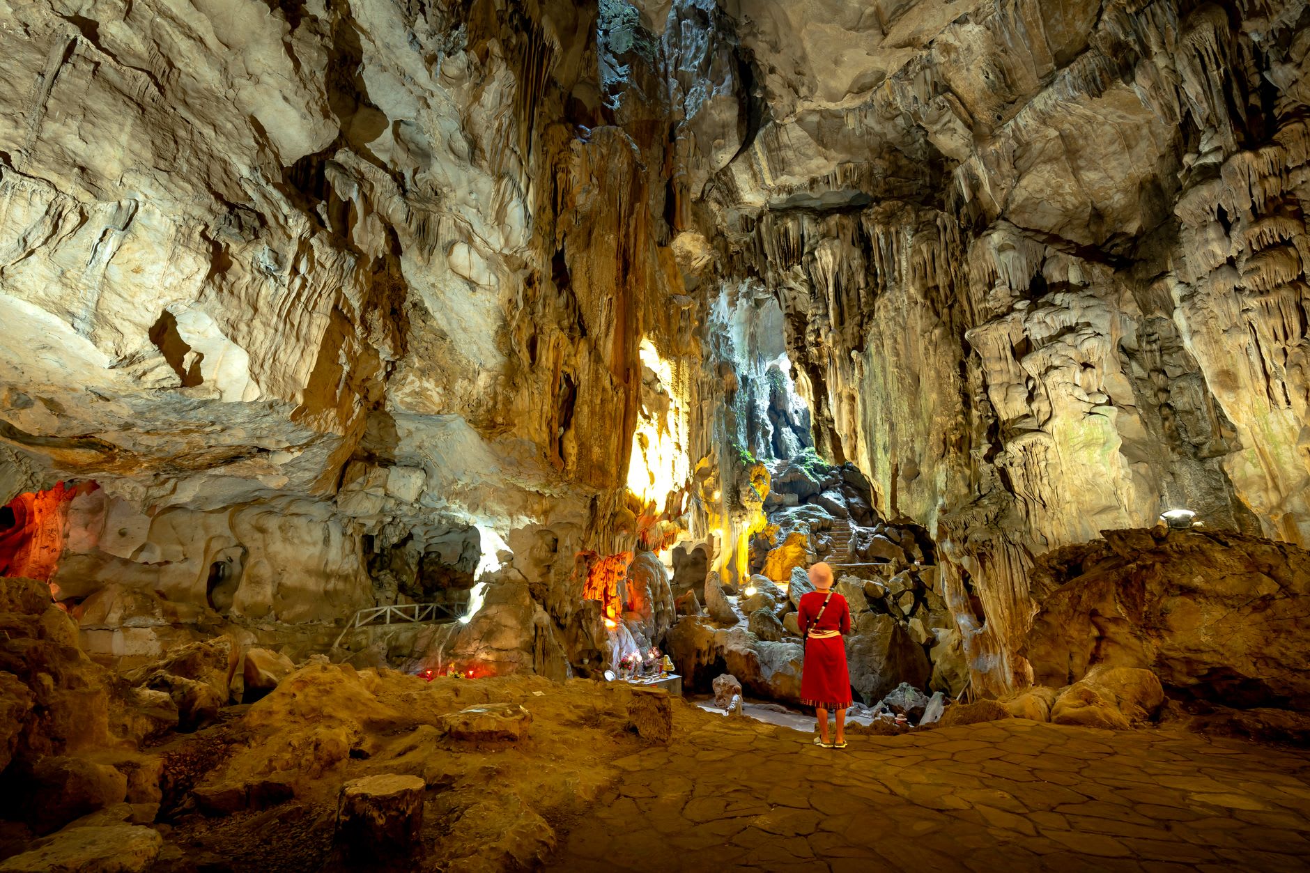 Formations massives de stalactites dans la Grotte de la Flûte de Roseau captant une lumière multicolore, reflétées dans un lac souterrain parfaitement immobile en dessous