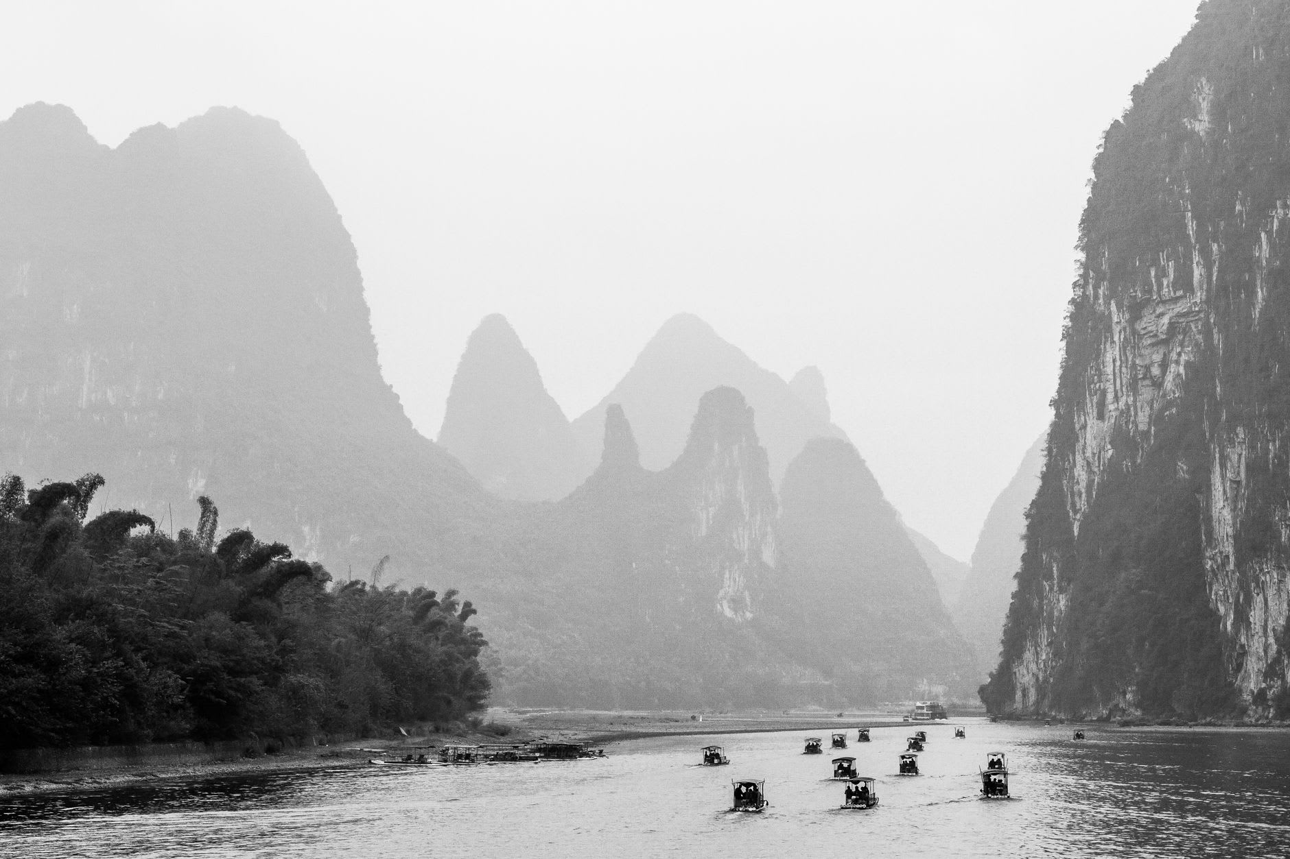 Traditional stone arch bridge spanning the Yulong River with bamboo groves and karst peaks framing the scene