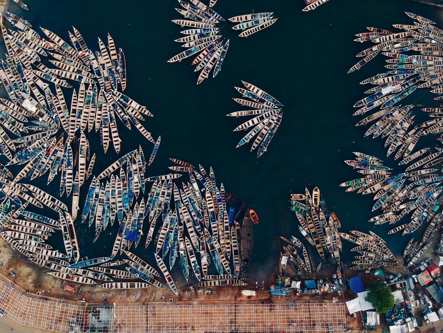 Women selling produce at Bandim market before sunrise, baskets of dried shrimp stacked in vivid orange-red mounds