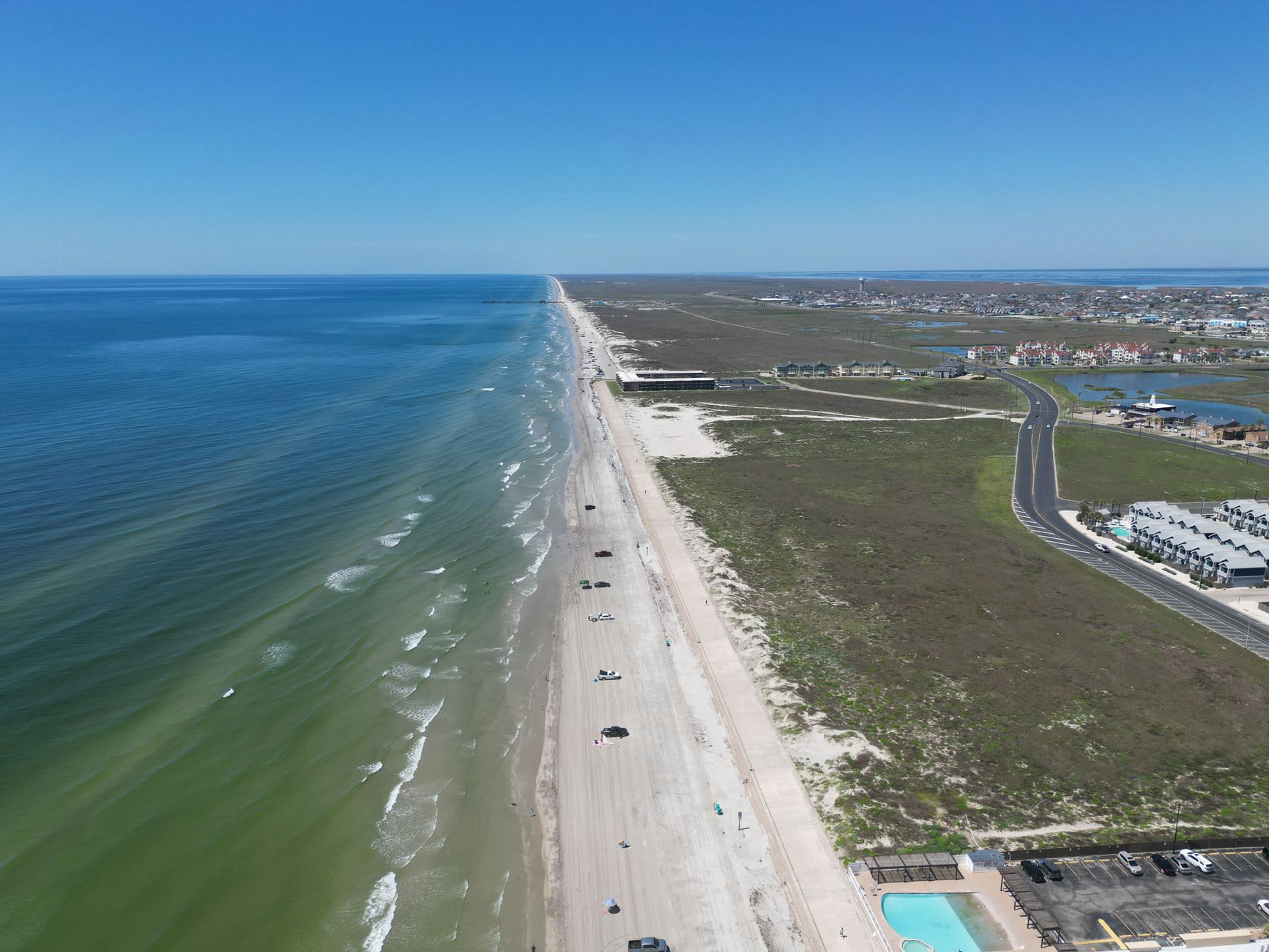Miles of empty Mustang Island beach stretching south at low tide, a surf fisherman in the far distance