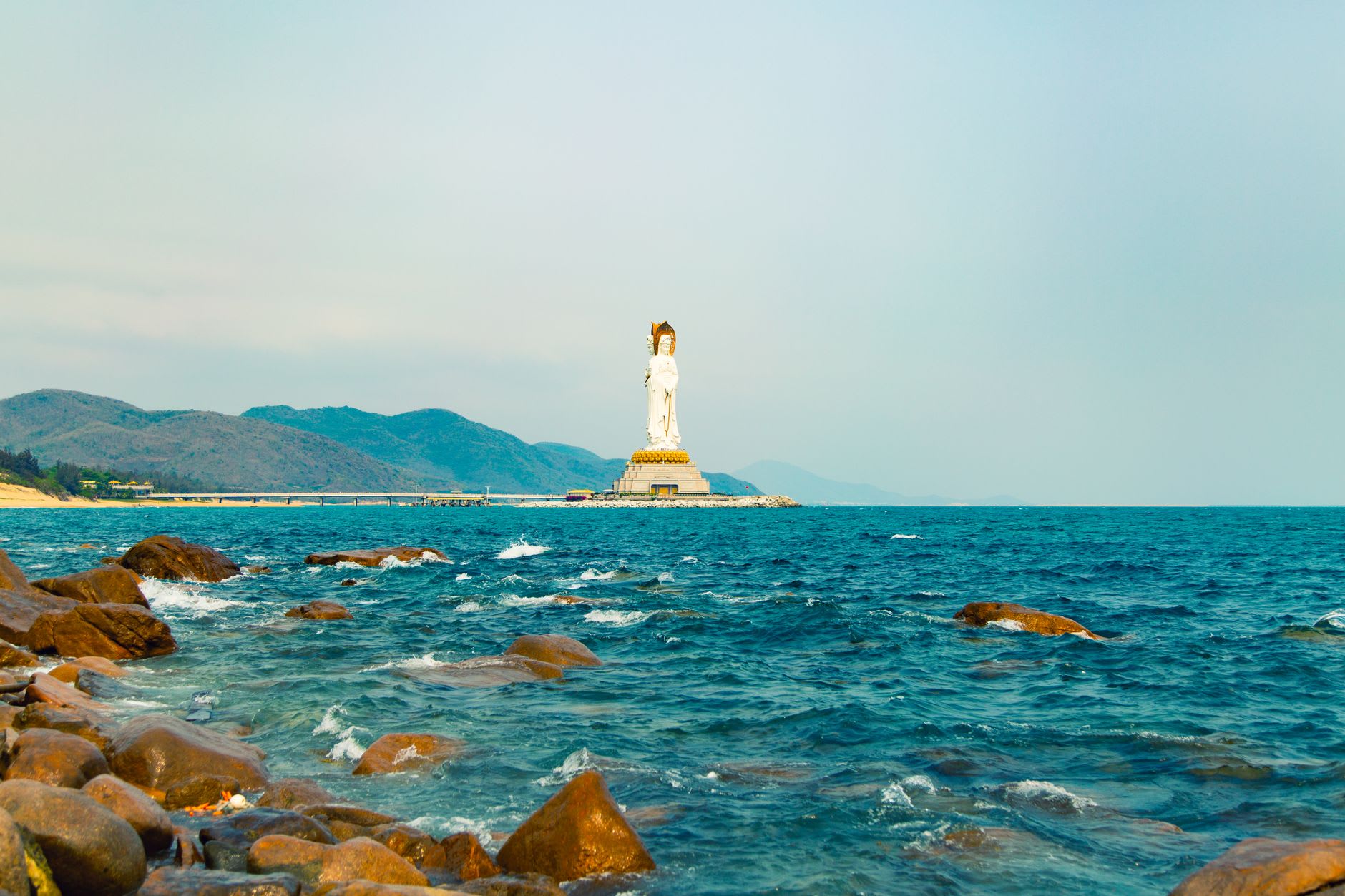Dark volcanic basalt rock formations at the southern end of Shimei Bay, waves breaking white against the black stone in late afternoon light