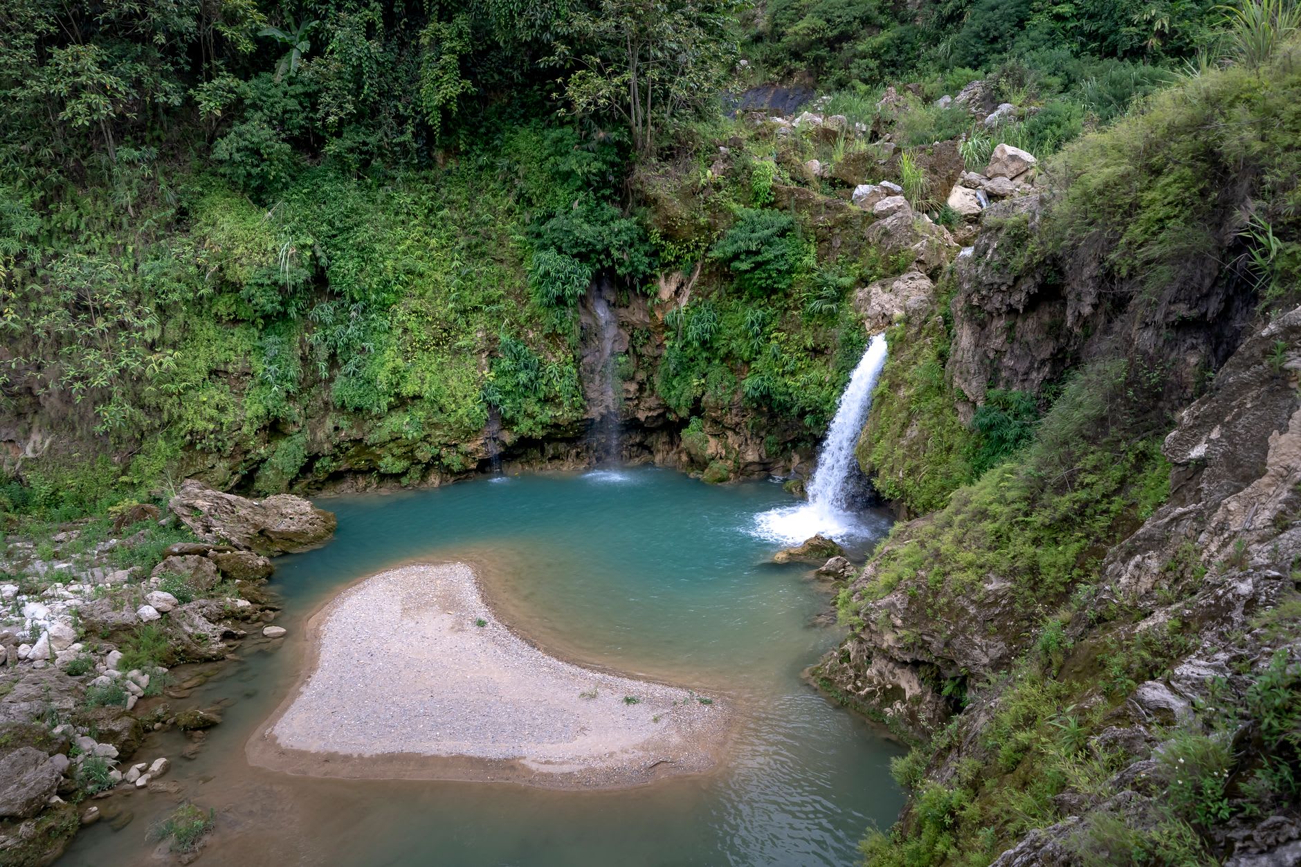 The crystal-clear blue water of the upper pool at Bassin Bleu reflecting the surrounding jungle