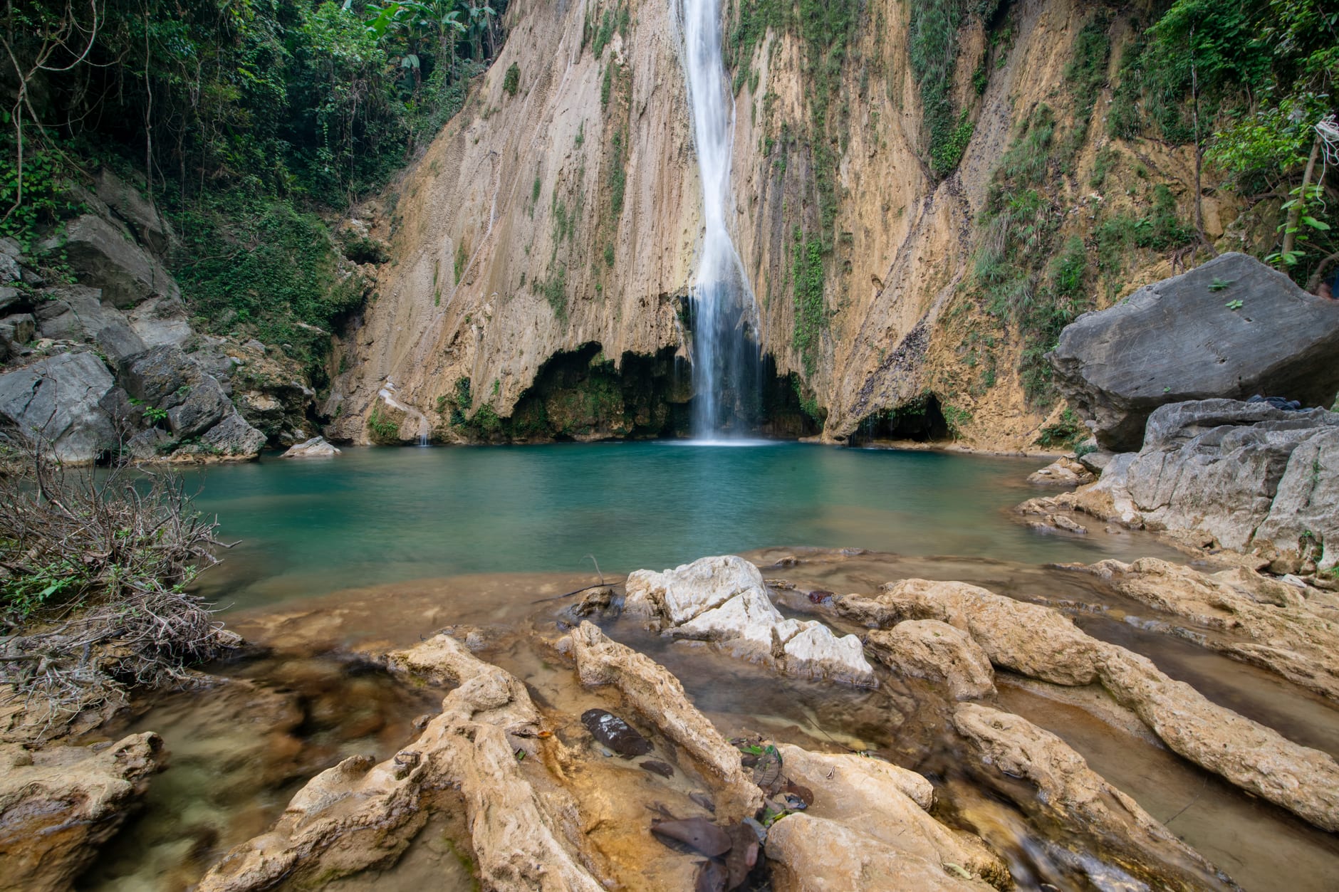 Visitors swimming in the emerald-blue water at Bassin Bleu while a waterfall cascades into the upper pool