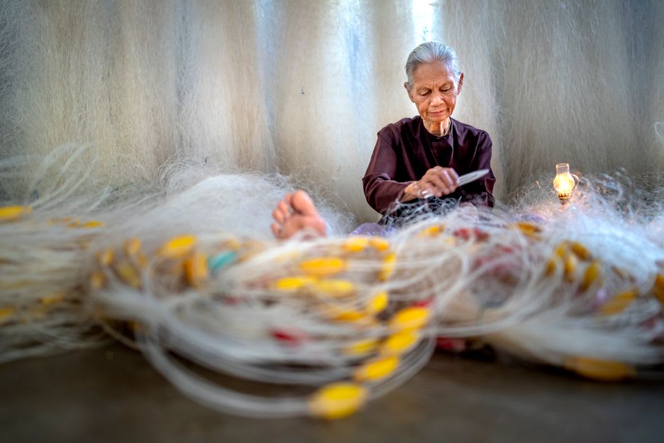 A woman mending fishing nets outside a small house on Île de la Tortue at dusk