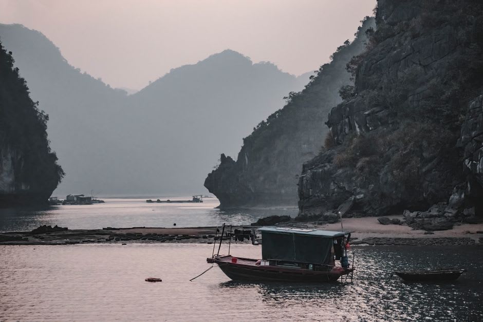 Wooden fishing boat drifting near stilted houses in the still water of Ba Hang lagoon