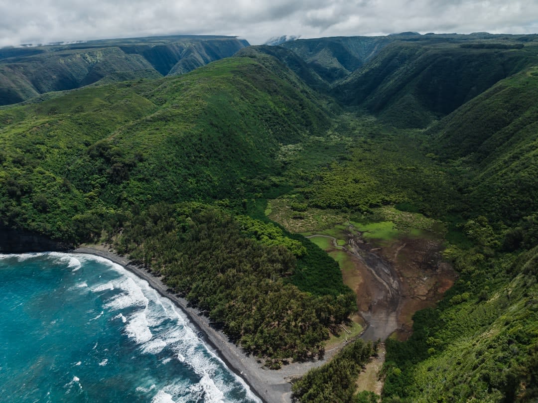 Sweeping view into the Kalalau Valley from Kalalau Lookout with fluted green ridges and clouds parting to reveal the ocean beyond