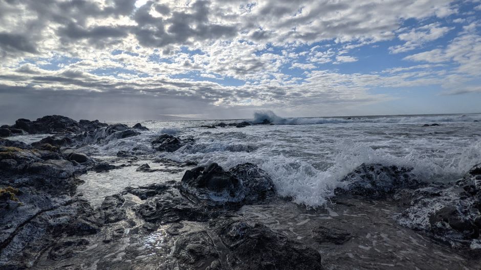 Windsurfers and kitesurfers riding waves off Hookipa Beach near Paia with Maui's coastline behind them