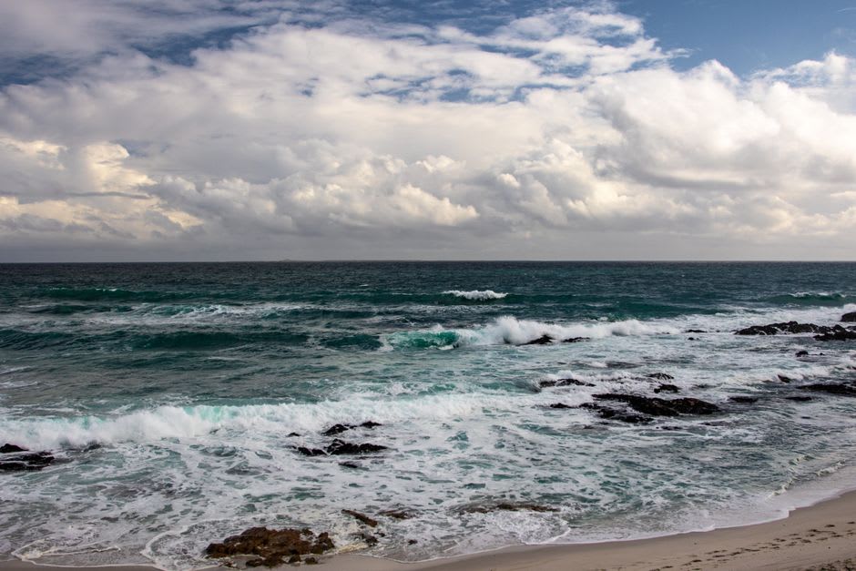 Des vagues s'écrasant contre le récif de roche noire exposé s'étendant depuis le cap Erimo, le vent fouettant visiblement la surface de l'eau