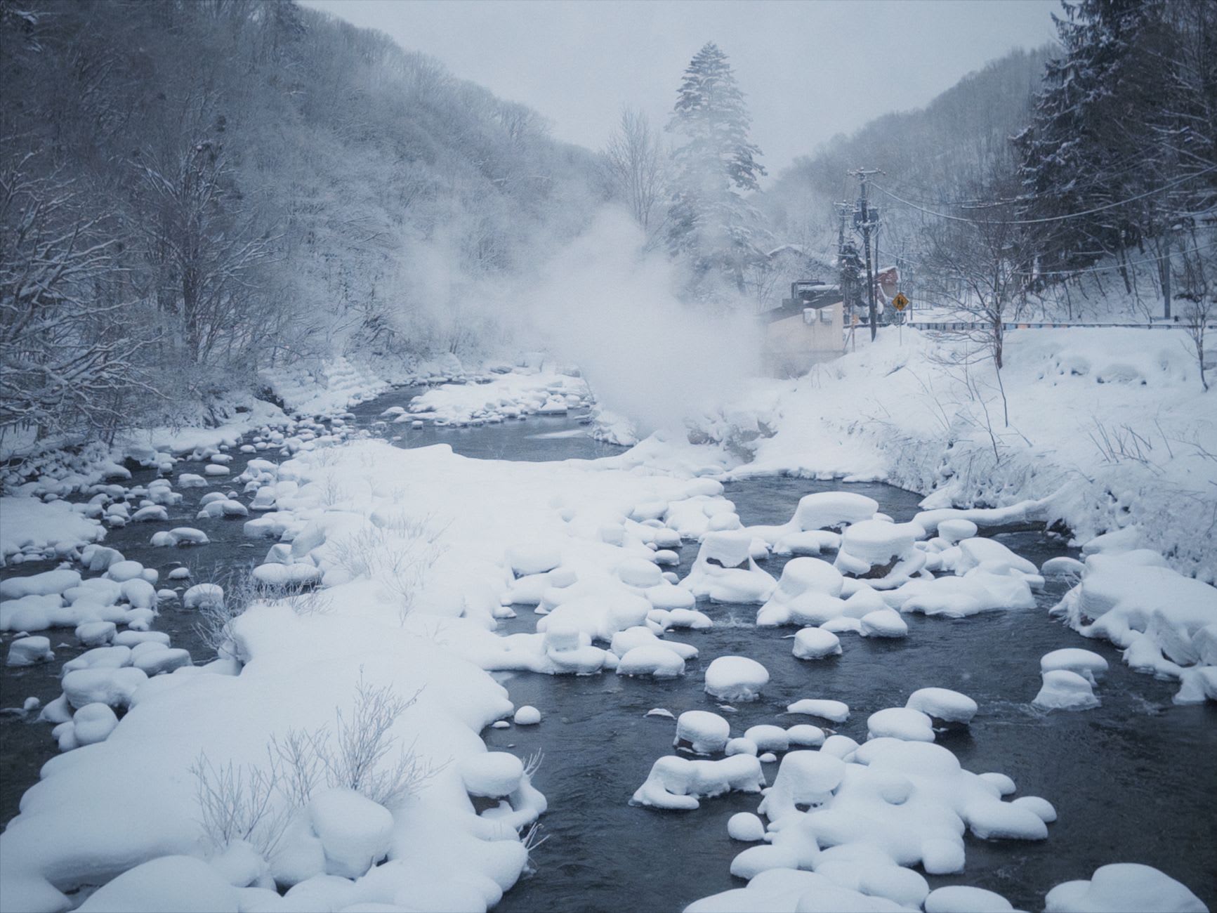 Jigokudani in Noboribetsu, the volcanic valley floor showing boiling mineral pools in pale green and white surrounded by grey sulfurous rock, steam rising into cold air