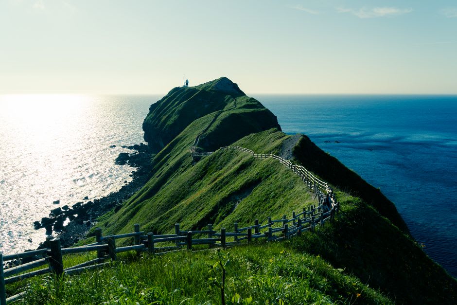 The narrow cliff-top trail at Cape Kamui with the intensely blue Shakotan waters visible on both sides and the lighthouse ahead