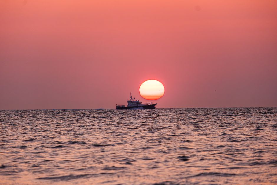 A fishing boat working the deep blue waters off the Shakotan coastline near sunset, cliffs rising in the background