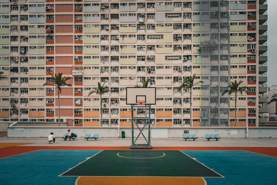 A pickup basketball game in progress on the rainbow-striped court at Choi Hung Estate, pastel towers rising around it