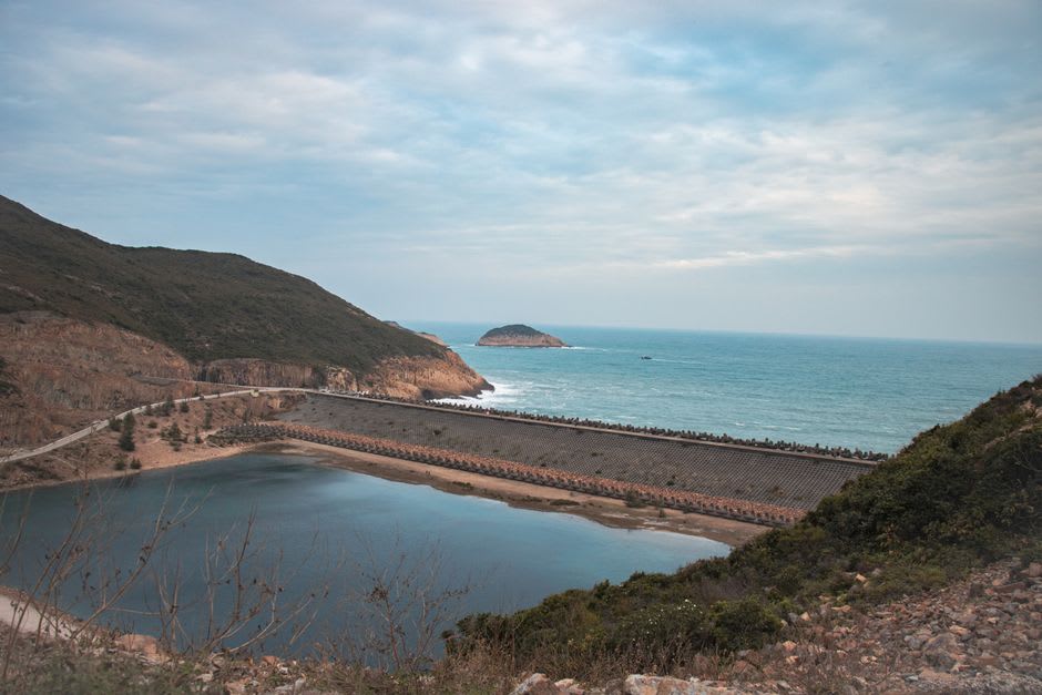 A narrow sea inlet cutting between hexagonal rock walls near High Island Reservoir, the water a deep turquoise