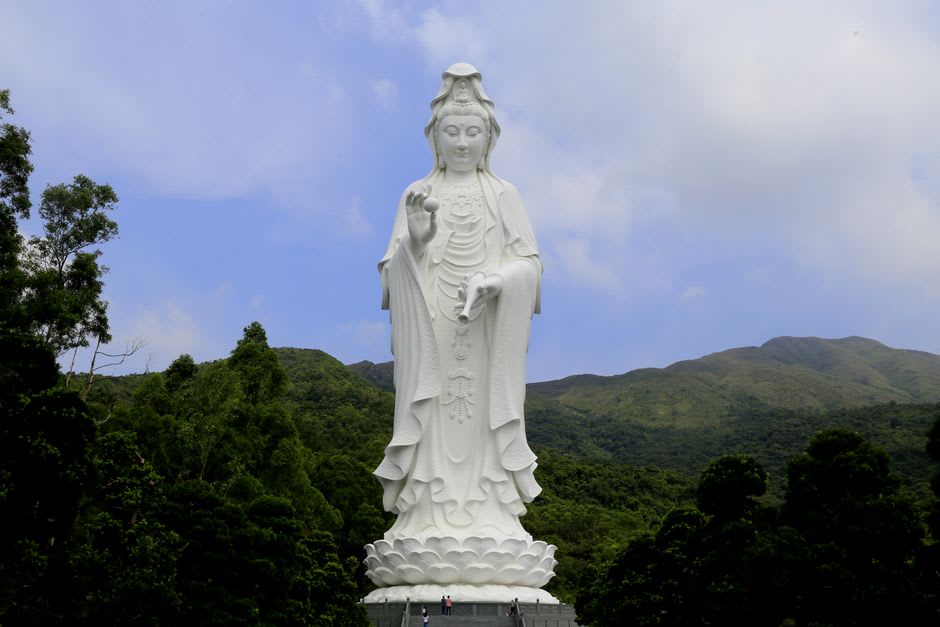 La estatua de bronce blanco de Guanyin vista desde el patio principal del monasterio, colinas boscosas alzándose detrás