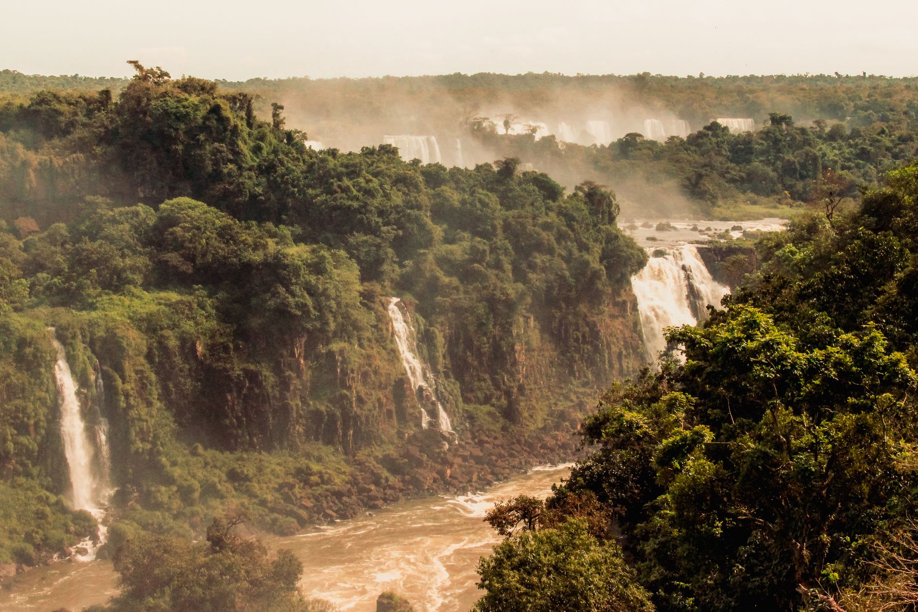 The full sweeping panorama of the Iguazú Falls seen from the main elevated walkway on the Brazilian side, showing the scale of the entire falls system