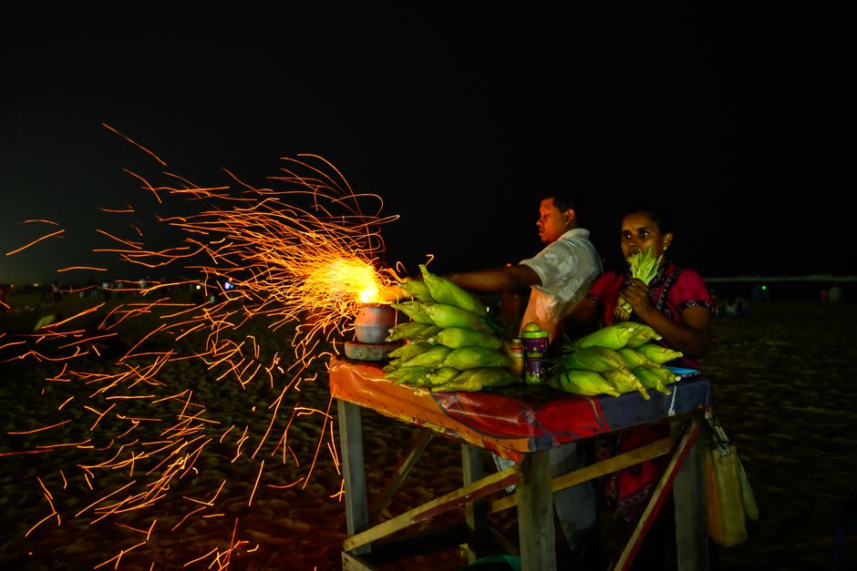 A charcoal-grilled corn vendor working the sand at a quiet Alibaug beach at sunset