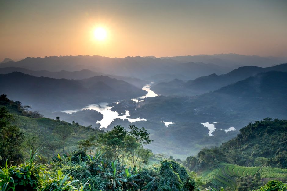 A misty morning view over the Dzukou Valley river winding between soft green hills
