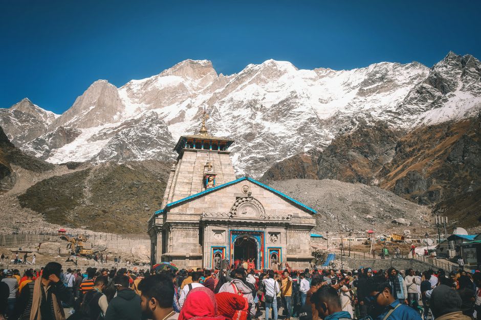 Pilgrims gathered at dusk outside Kedarnath temple with oil lamps lit along its edge