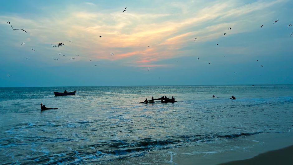 Panambur Beach at dusk with fishing catamarans on the sand and cargo ships anchored offshore