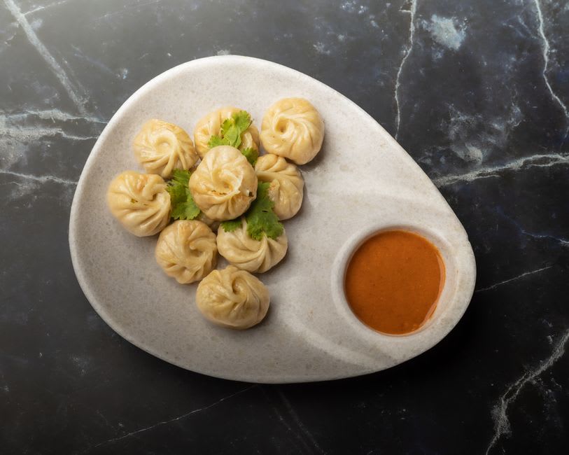 A steaming plate of Tibetan momos served with red chilli sauce at a mountain café