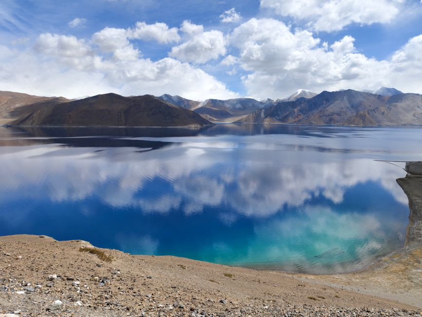 Pangong Lake's water shifting between turquoise and deep blue along its rocky shore