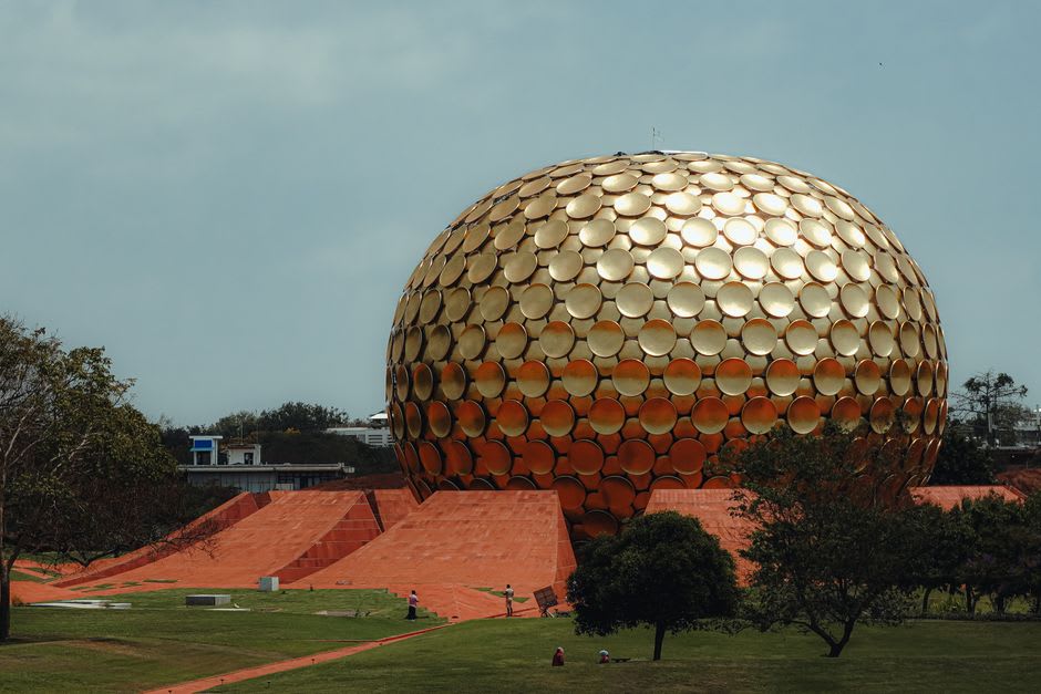 The golden geodesic Matrimandir at Auroville rising above the surrounding forest at dusk