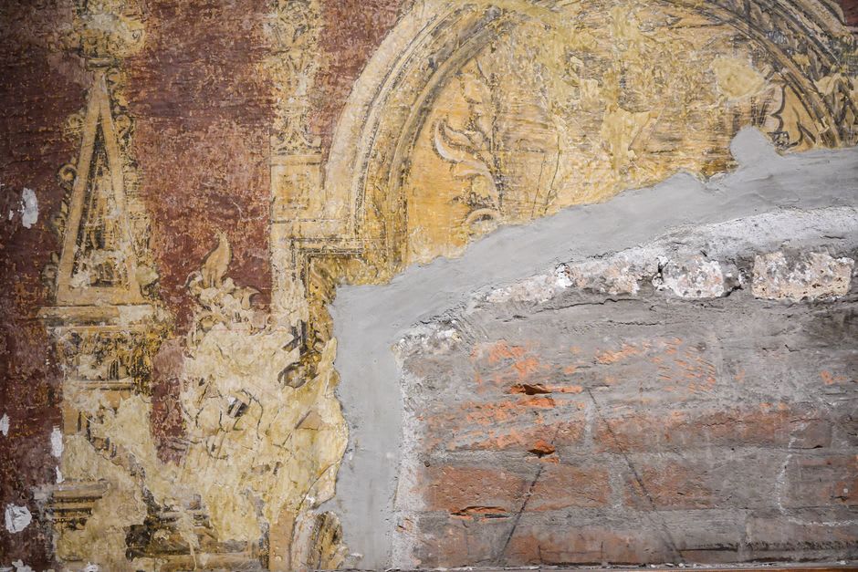 A weathered Shekhawati haveli facade covered in fresco panels of trains, gods, and processions
