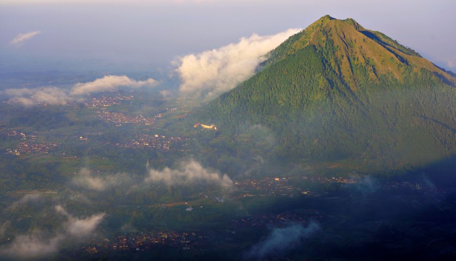 Sunrise view over misty hills and volcanic peaks from above Batu
