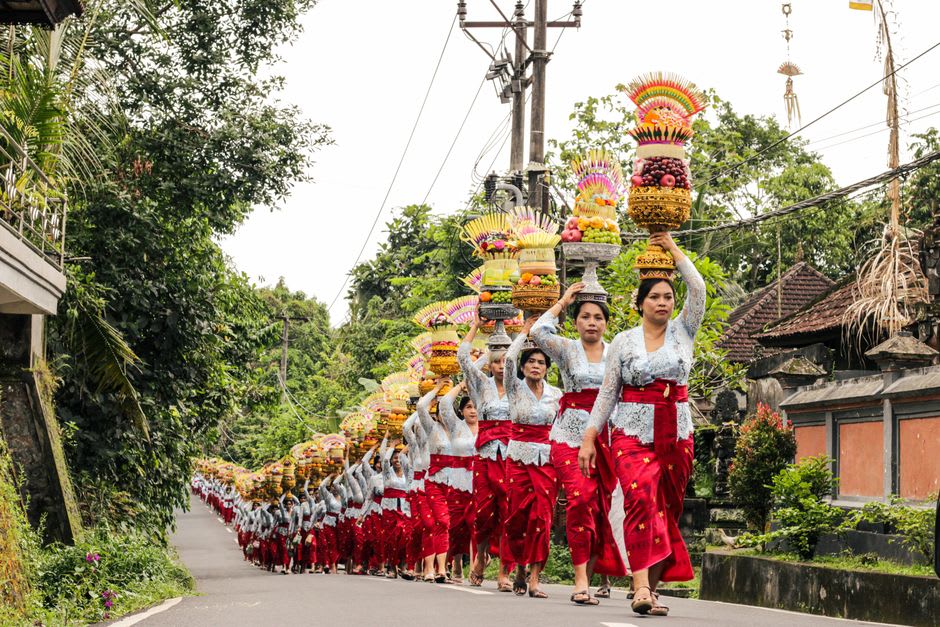 Balinese women carrying tall gebogan fruit offerings up temple steps during a ceremony at Besakih