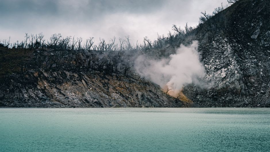 Steam rising off the turquoise sulfur waters of Kawah Putih crater lake