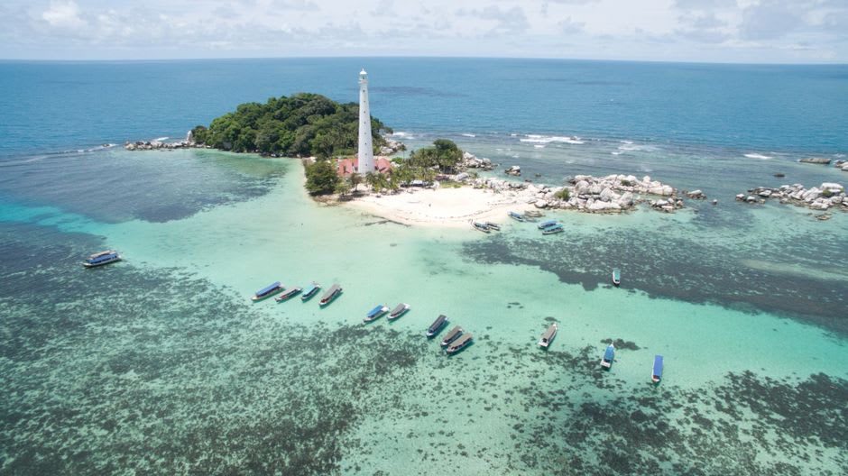 The historic white lighthouse on Lengkuas Island surrounded by granite boulder coastline
