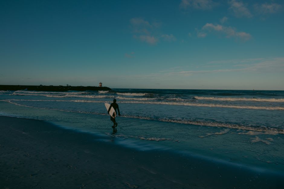 Surfers paddling out at sunset over the black volcanic sand break at Echo Beach
